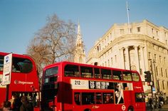 two red double decker buses parked in front of a tall building on a city street