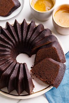 a chocolate bundt cake on a plate with two cups of coffee