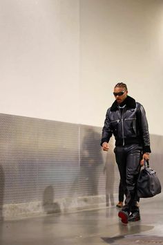 a man in black jacket and sunglasses walking down a hallway with a handbag on his hip