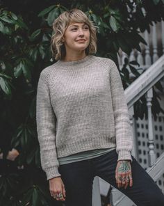 a woman standing in front of a tree with her hands on her hips, wearing a sweater and jeans