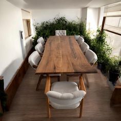 a wooden table surrounded by white chairs and potted plants