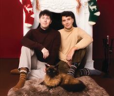 two men sitting next to each other in front of a fire place with a cat