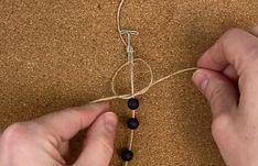 two hands are stringing together beads on a piece of wood and sand, while another hand is holding the bead