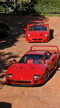 three red sports cars are parked on the side of a brick road in front of some bushes