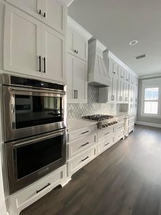 an empty kitchen with white cabinets and stainless steel ovens, wood flooring, and hardwood floors