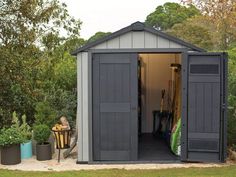 a small shed with its door open and some plants in the back ground next to it