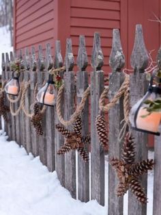 some pine cones are hanging from a wooden fence with lights on it and snow in the foreground