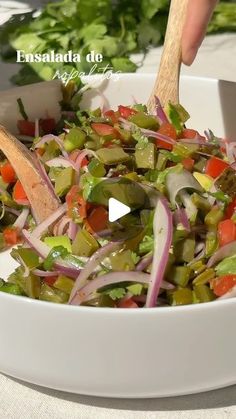 a white bowl filled with lots of veggies on top of a table next to a wooden spoon