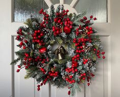 a christmas wreath hanging on the front door with bells and evergreen leaves, red berries and pine cones