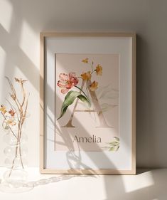 a vase with flowers sitting on top of a table next to a framed letter art print