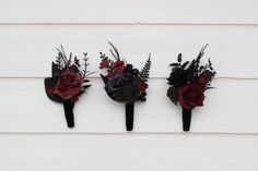 three boutonnieres with red and black flowers are on a white board wall