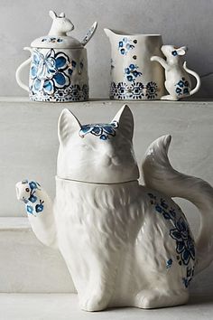 a white cat figurine sitting on top of a shelf next to two teapots