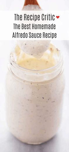 a jar filled with homemade alfredo sauce on top of a white table next to a wooden spoon