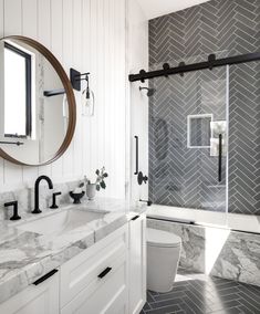 a white bathroom with marble counter tops and black accents on the shower door, along with a round mirror above the sink