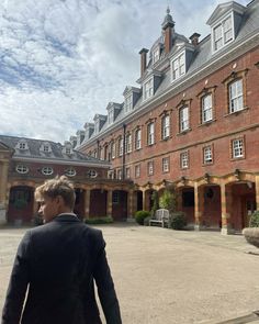 a man is walking in front of a large red brick building with many windows on it