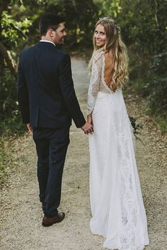 a man and woman holding hands walking down a dirt road