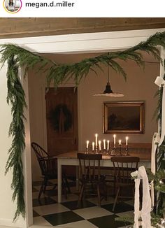 a dining room decorated for christmas with greenery on the table and candles in the center