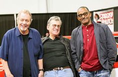 three men standing next to each other in front of a red and white truck at an auto show