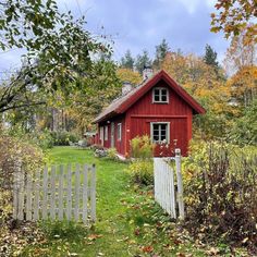 a red house with a white picket fence in the foreground and autumn foliage around it