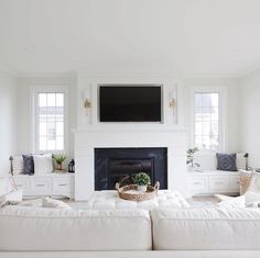 a living room with white furniture and a flat screen tv on the fireplace mantel