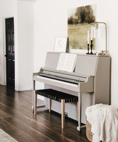 a piano sitting on top of a hard wood floor in a living room next to a painting