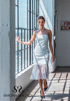 a woman in a dress is walking down the sidewalk near a window with her hand out