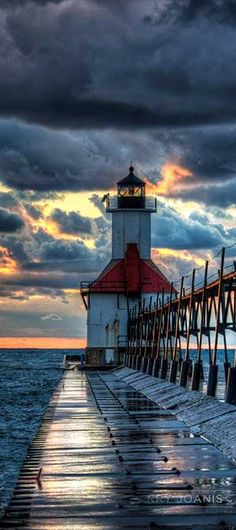 a light house sitting on top of a pier next to the ocean under a cloudy sky