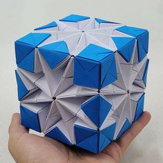 a hand holding a blue and white origami cube