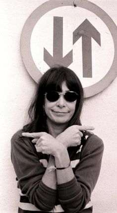 black and white photograph of a woman with sunglasses pointing at the sign that says no left turn