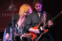 a man and woman playing guitars on stage with microphones in front of them,