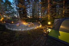 a tent is set up in the middle of a wooded area with benches and lights