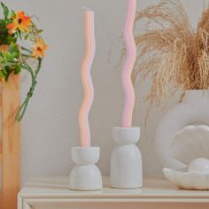 two white vases sitting next to each other on top of a table with flowers in the background