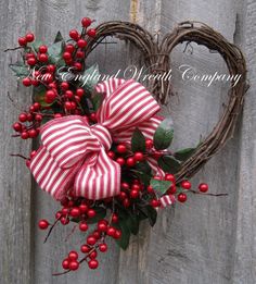 a heart shaped wreath with red berries and greenery tied to it, hanging on a wooden fence