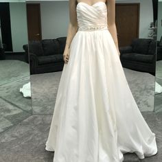 a woman standing in front of a mirror wearing a white wedding dress with beaded waist