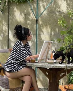 a woman sitting at a table with a cat in front of her and an easel next to her