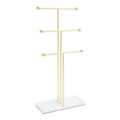 a white and gold coat rack with three hooks on it's sides, in front of a white background