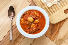 a bowl of soup on a wooden table next to a cutting board with silverware