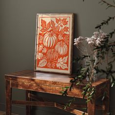 an orange and white art piece sitting on top of a wooden table next to a vase with flowers