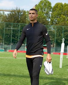 a man walking across a lush green field holding a soccer ball in his right hand