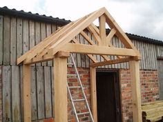 a wooden structure with a ladder in front of it and a brick building behind it