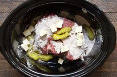 a slow cooker filled with meat and vegetables covered in powdered sugar, sitting on a wooden table