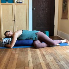 a woman laying on top of a blue mat in a room with wooden floors and cabinets