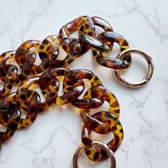 This trendy acrylic chain in Tortoise color features a classic brown dimple print that complements any outfit! With two adjustable O-rings, you can easily shorten the chain to your preferred length. It's the perfect blend of style and versatility, effortlessly matching everything in your wardrobe. Specifications:- 23.5" long without the O-rings- 26.5" long with the O-rings Trendy Adjustable Tortoiseshell Jewelry, Brown Chain Jewelry As Fashion Accessory, Trendy Brown Chain Jewelry, Tortoise Print, Acrylic Bag, Tortoise Color, Classic Brown, Bag Chain, Pull Apart