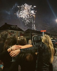 two women hug each other as fireworks go off in the background