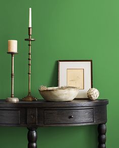 a wooden table topped with a bowl next to a candle and framed pictures on the wall