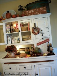 an old fashioned kitchen with white cabinets and pumpkins on the top shelf above it