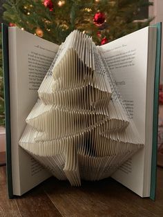 an open book with folded pages in front of a christmas tree