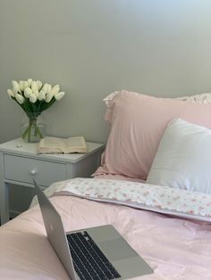 a laptop computer sitting on top of a bed next to pillows and a vase with flowers