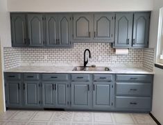 an empty kitchen with gray cabinets and white marble counter tops, black faucet