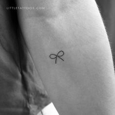 a small bow tattoo on the left inner arm, with an arrow in the middle